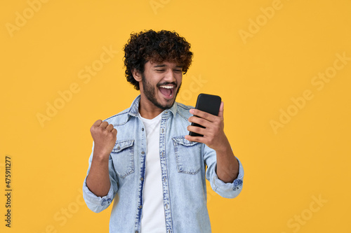 Foto Excited happy young indian man winner feeling joy using smartphone winning lottery game, betting, getting cashback online gift in mobile app message holding cell phone isolated on yellow background