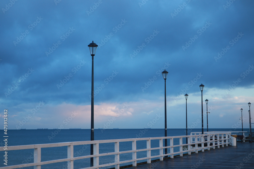 Pier on the Baltic Sea. Many birds on the sea and a wooden pier. There are many lanterns on the pier. A flock of birds over the sea.