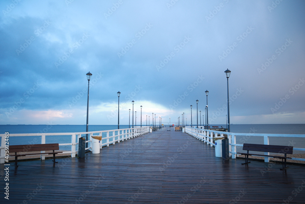 Pier on the Baltic Sea. Many birds on the sea and a wooden pier. There are many lanterns on the pier. A flock of birds over the sea.