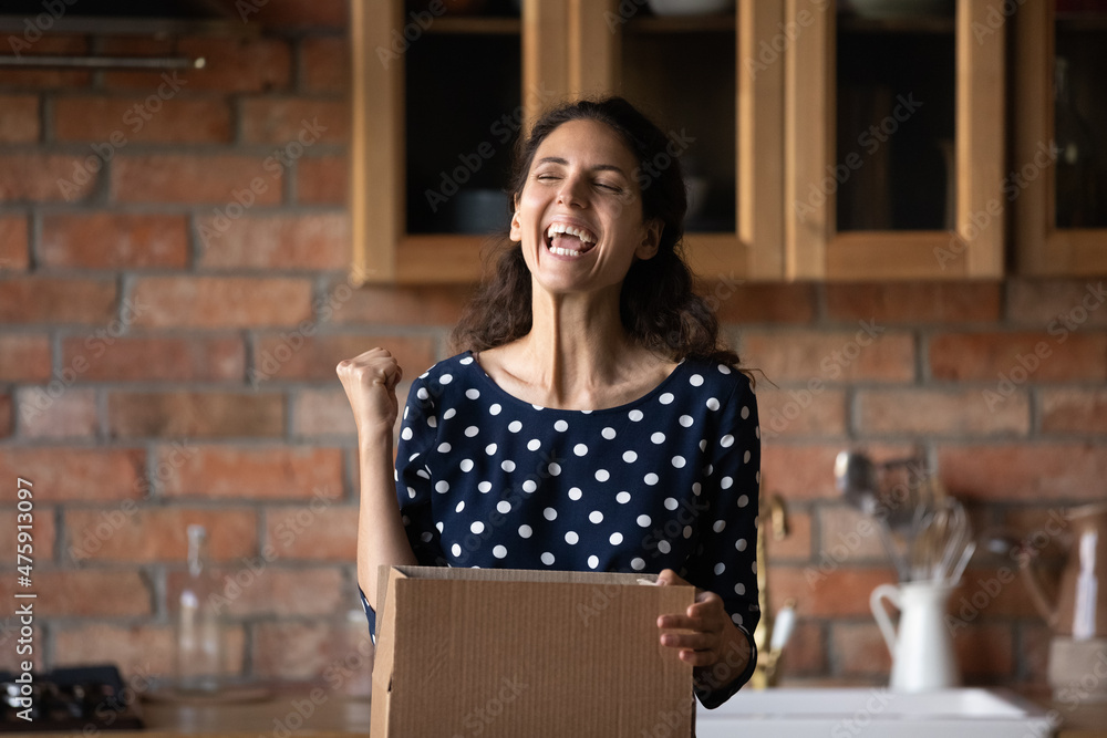 Emotional happy young hispanic woman unpacking huge cardboard box, feeling excited of getting wished item from internet store or receive online lottery auction prize, satisfied with fast delivery.