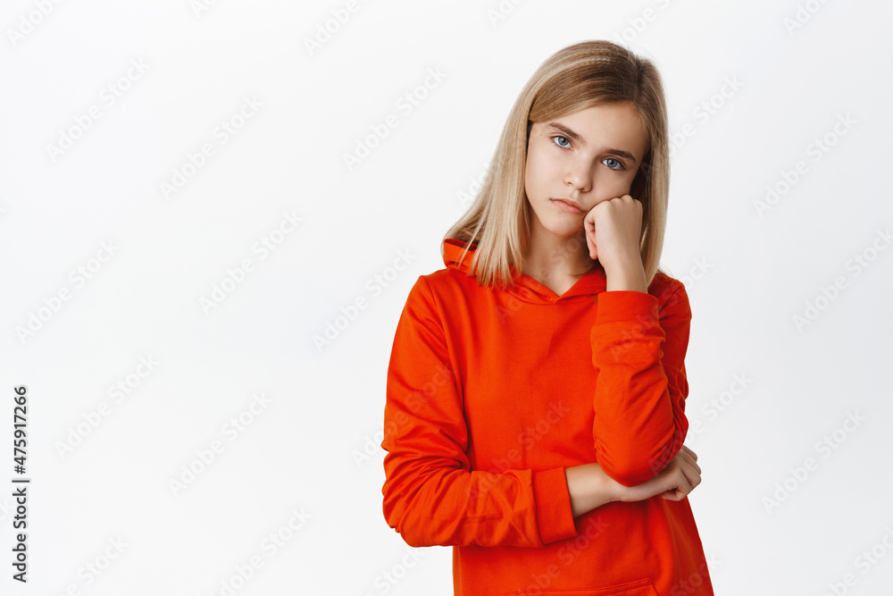 Bored little girl looking with sad, gloomy and unamused face at camera, standing upset and moody against white background Bored little girl looking with sad, gloomy and unamused face at camera, standing upset and moody against white background