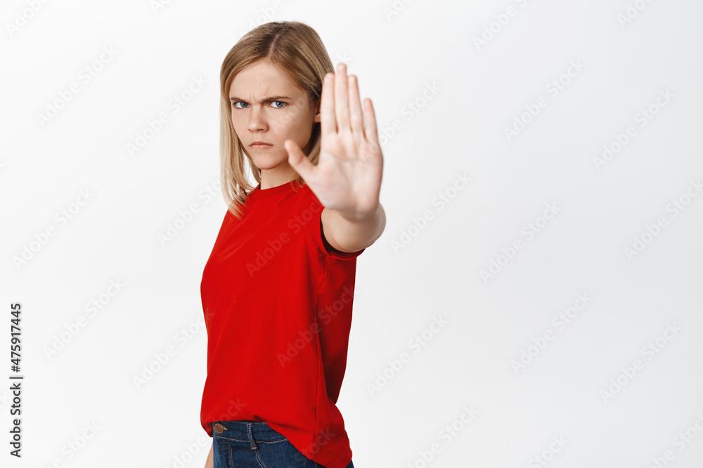 Serious little kid, girl extends one hand, shows stop, taboo or block gesture, prohibit and say no, standing over white background Serious little kid, girl extends one hand, shows stop, taboo or block gesture, prohibit and say no, standing over white background