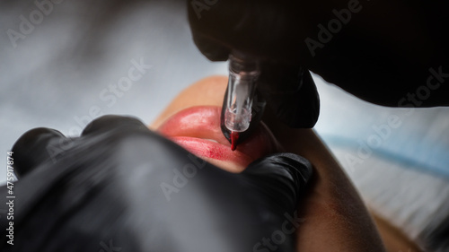 Cosmetologist in black gloves making permanent makeup on woman's lips with tattoo pen machine. Microblading process