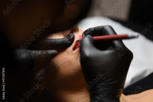 Closeup photo of the process of applying permanent makeup tattoo of woman red lips