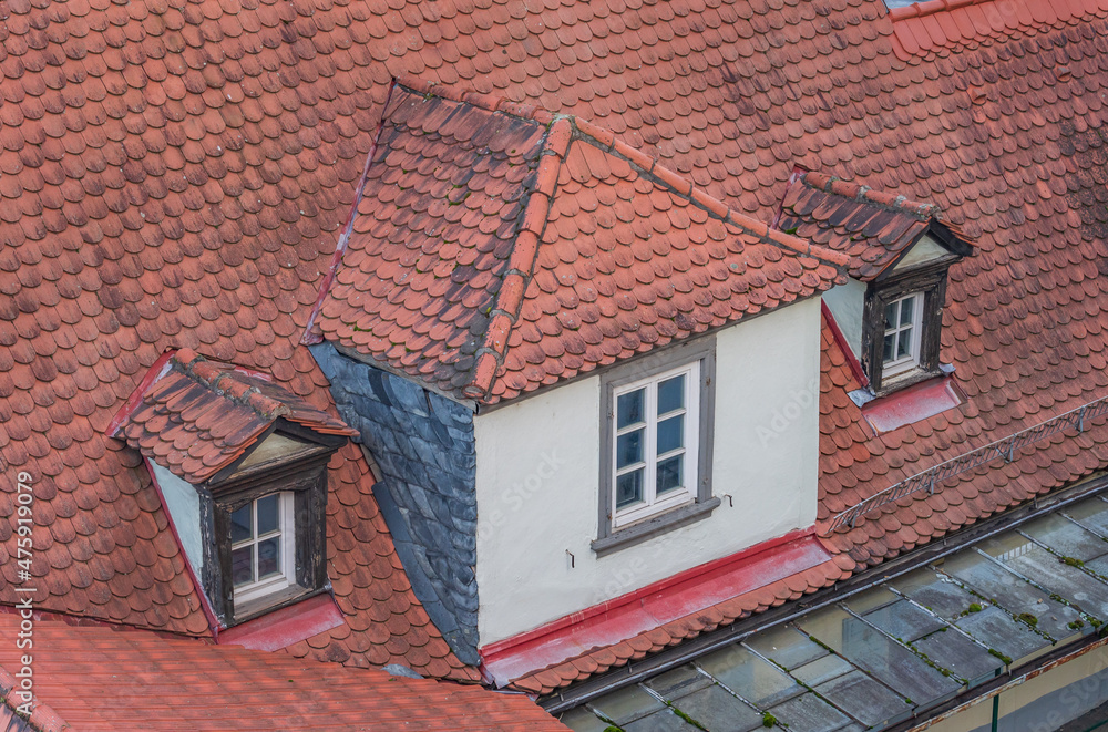 Three windows in a red-tiled roof of an old building in Europe