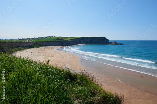 A beach surrounded by cliffs and vegetation under a clear sky.