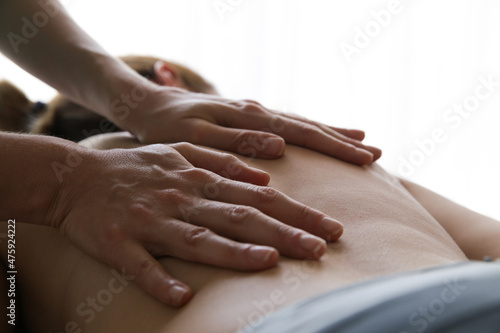 Close up of professional masseuse hands massaging her female client back at relax ambient.