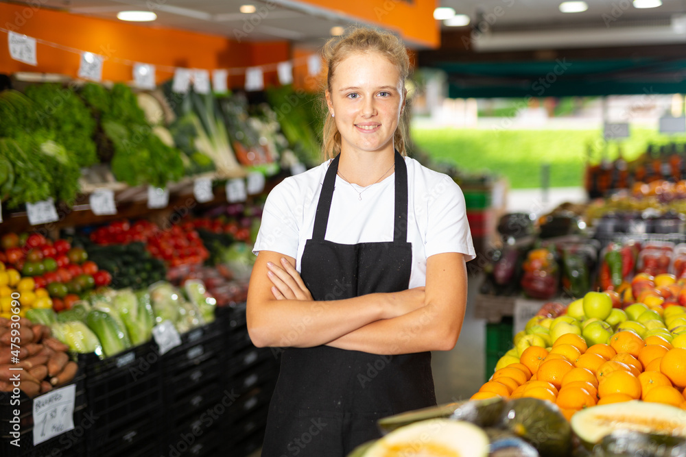 Waist up portrait of pretty young saleswoman posing with fresh fruits and vegetables at grocery store