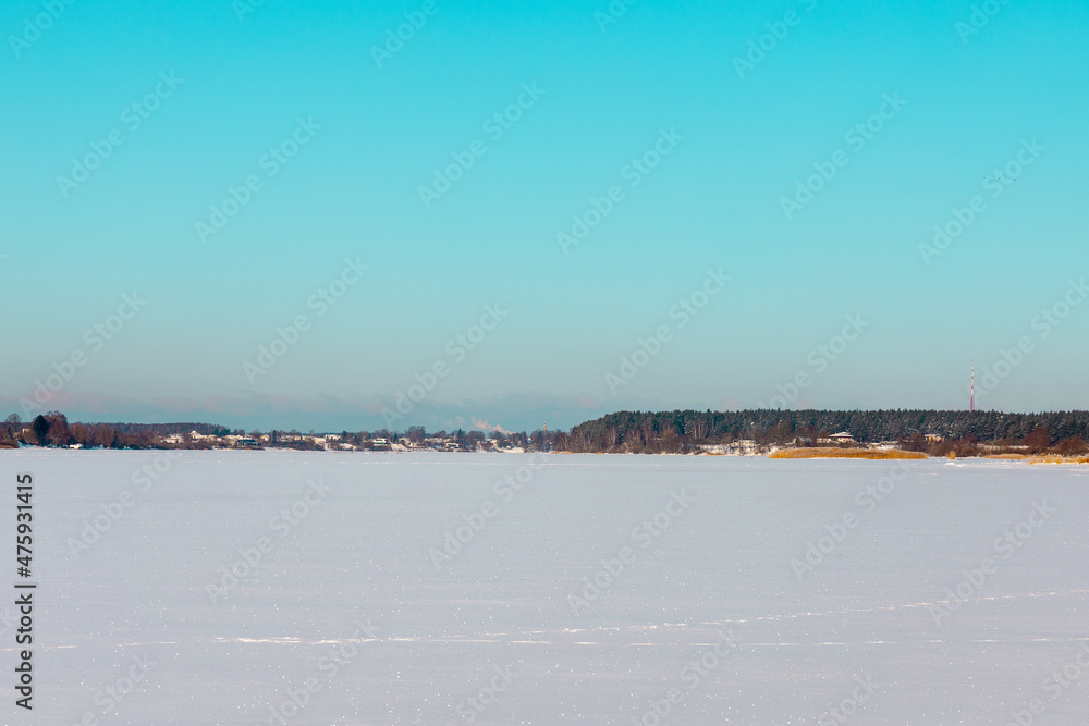 Winter landscape with ice covered lake or river with shores and clear sky