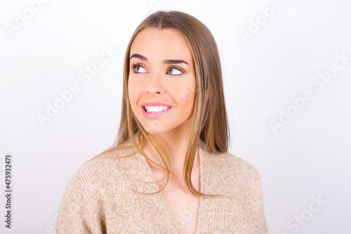 Amazed young caucasian girl wearing knitted sweater over white background bitting lip and looking tricky to empty space.