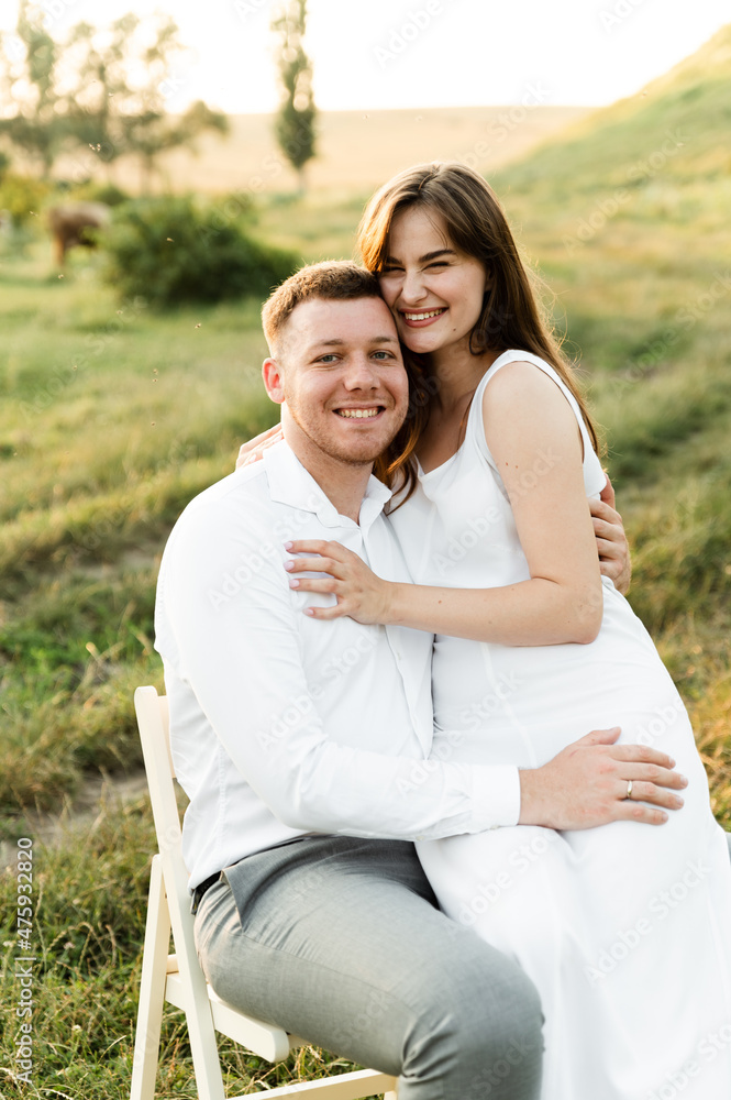 the newlyweds are sitting on a chair and hugging tenderly. girl with a boyfriend on a romantic date at sunset of the day. beautiful couple in the field. the newlyweds are sitting on a chair and hugging tenderly. girl with a boyfriend on a romantic date at sunset of the day. beautiful couple in the field.