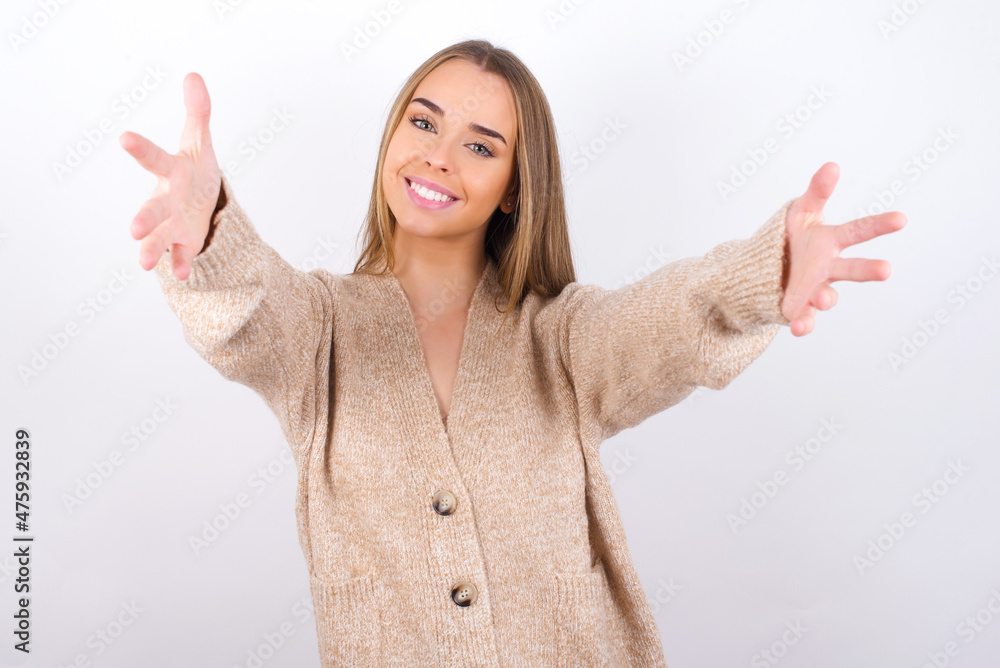 young caucasian girl wearing knitted sweater over white background looking at the camera smiling with open arms for hug. Cheerful expression embracing happiness. young caucasian girl wearing knitted sweater over white background looking at the camera smiling with open arms for hug. Cheerful expression embracing happiness.