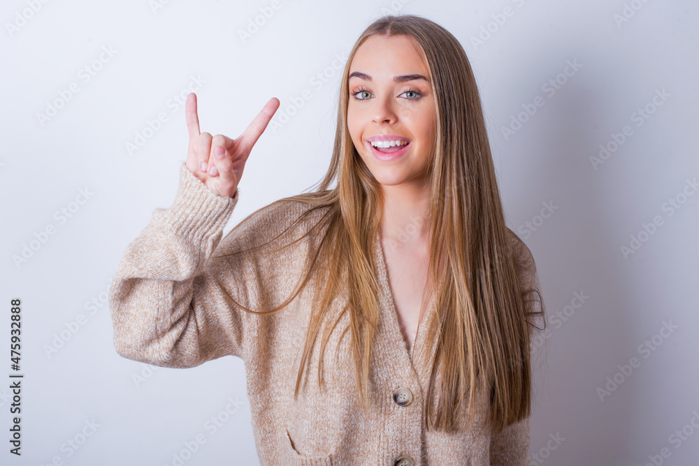 young caucasian girl wearing knitted sweater over white background doing a rock gesture and smiling to the camera. Ready to go to her favorite band concert. young caucasian girl wearing knitted sweater over white background doing a rock gesture and smiling to the camera. Ready to go to her favorite band concert.