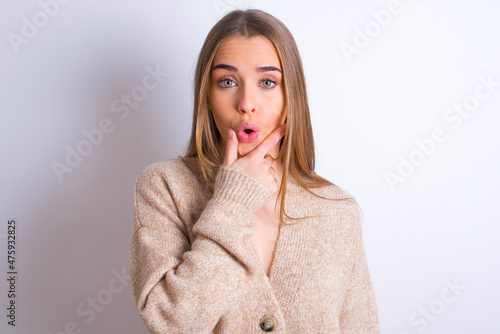 young caucasian girl wearing knitted sweater over white background Looking fascinated with disbelief, surprise and amazed expression with hands on chin