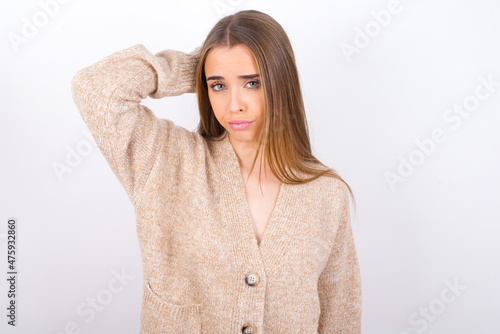 young caucasian girl wearing knitted sweater over white background confuse and wonder about question. Uncertain with doubt, thinking with hand on head. Pensive concept. © Roquillo