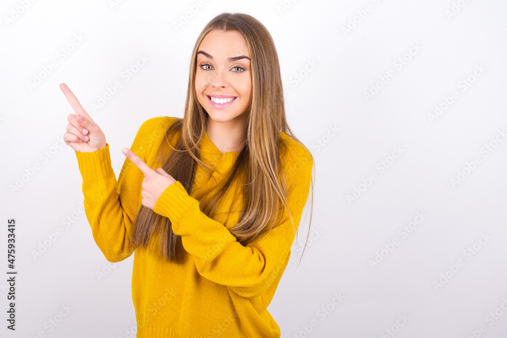 Young caucasian girl wearing yellow sweater over white background points at copy space indicates for advertising gives right direction Young caucasian girl wearing yellow sweater over white background points at copy space indicates for advertising gives right direction