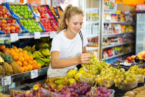 Young american girl choosing sweet grape at grocery section of supermarket