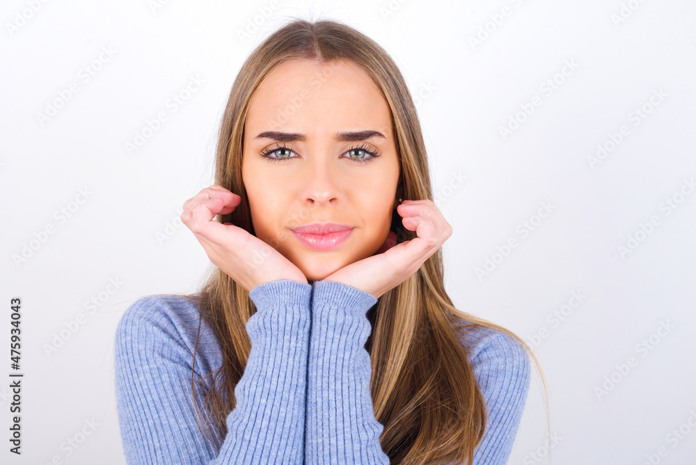 Portrait of sad Young caucasian girl wearing blue turtleneck over white background hands face Portrait of sad Young caucasian girl wearing blue turtleneck over white background hands face