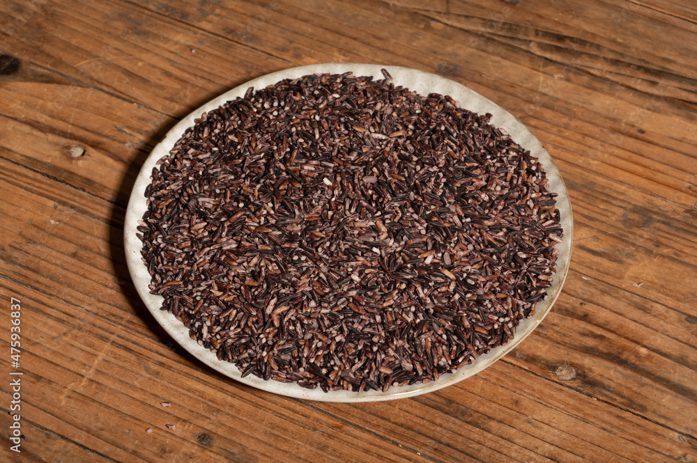 Place the black rice in the plate or bowl on the wood grain table Place the black rice in the plate or bowl on the wood grain table