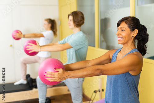 Young boy and girl standing in row with pilates trainer latin woman and using small fitness balls for exercising.