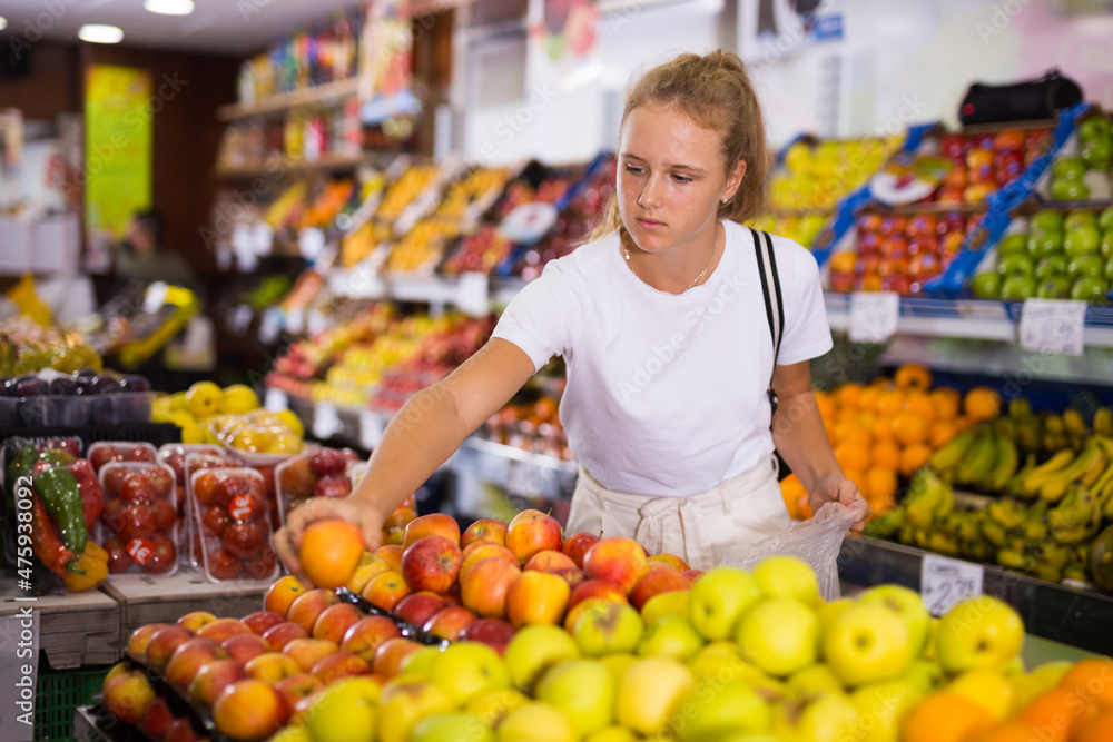 Young european woman purchaser choosing red organic apples in a grocery store