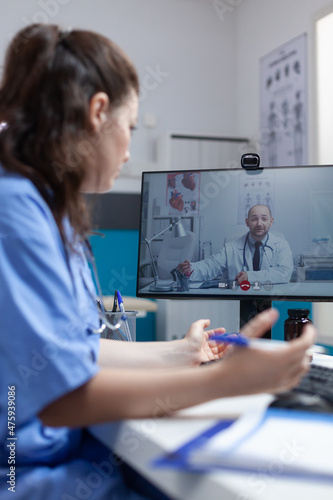 Physician nurse discussing virus symptoms with remote doctor during online videocall meeting conference during clinical consultation in hospital office. Telemedicine call on computer screen