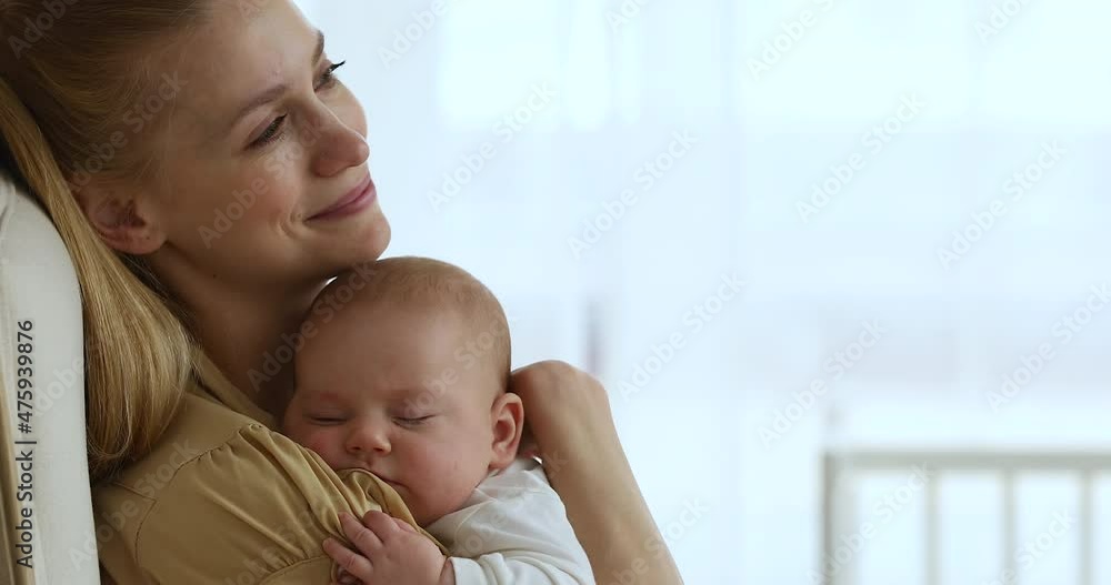 Happy serene mother sit in armchair cuddle caress tender baby napping on her shoulder look at distance dream of good health happy future for kid. Smiling relaxed mom guard sweet sleep of infant child Happy serene mother sit in armchair cuddle caress tender baby napping on her shoulder look at distance dream of good health happy future for kid. Smiling relaxed mom guard sweet sleep of infant child