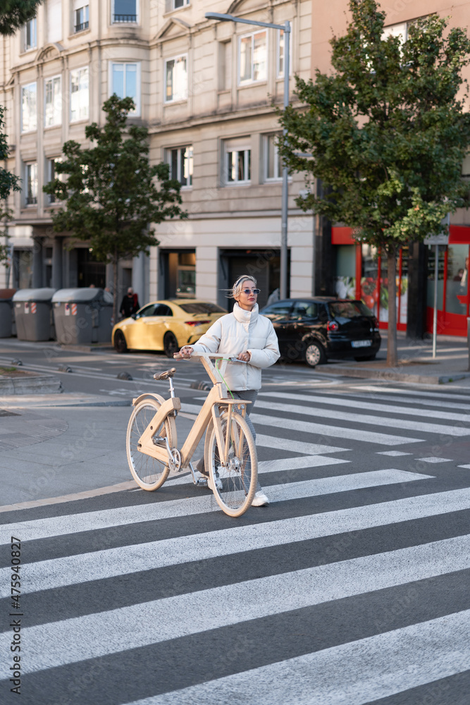 Trendy woman in outerwear cyclist crosswalk on city street.