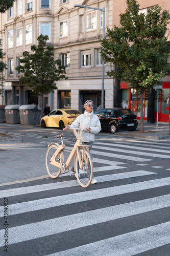 Trendy woman in outerwear cyclist crosswalk on city street.