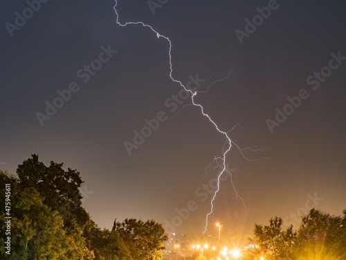 Long lightning strike over the city between green trees