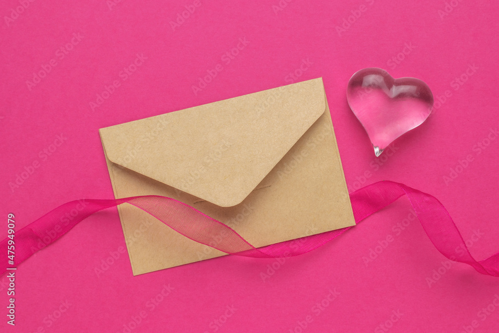 A postal envelope, a red ribbon and a glass heart on a crimson background. The concept of Valentine's Day. A postal envelope, a red ribbon and a glass heart on a crimson background. The concept of Valentine's Day.