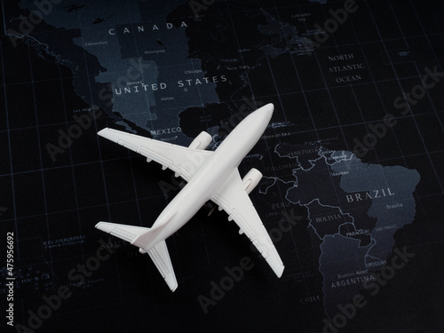Close-up white plane toy model on world map background, top view, minimal style. Flight, travel, destination, and journey concept.