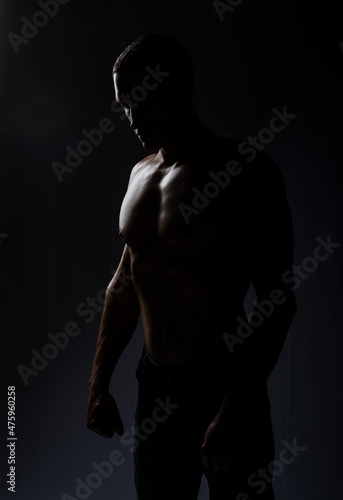 man posing in backlight. The model in the studio poses, demonstrates muscles, beautiful body relief. spot, healthy lifestyle. Black background. silhouette