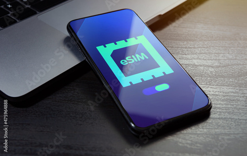 eSIM technology concept. Embedded SIM electronic phone sim card - mobile cellular global internet communication technology. Close up smartphone lying on a wooden table with an esim icon on the screen photo