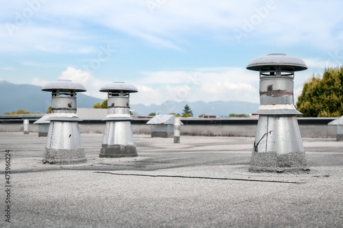 Flat roof vents on building with 2-ply SBS or modified bitumen roofing system. Group of metal ventilators such as: bathrooms and laundry exhaust and plumbing stack vent. Selective focus.