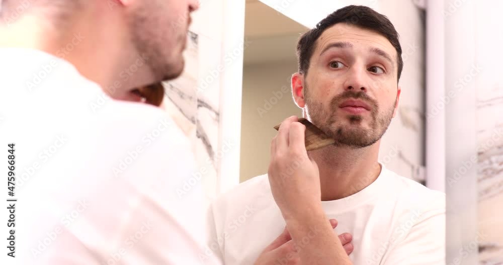 Handsome bearded man combing his beard while looking at himself in mirror after shower. Handsome bearded man combing his beard while looking at himself in mirror after shower.