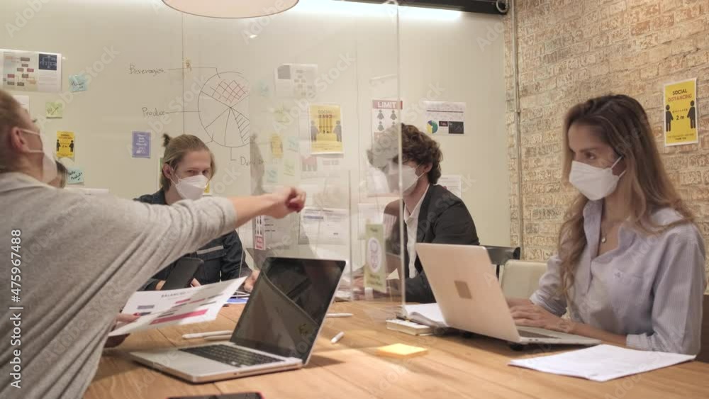 Multiracial business coworker team working in a new normal office. COVID-19 protection by cleared partition workplace, social distancing, and face mask for pandemic health and disease prevention. Multiracial business coworker team working in a new normal office. COVID-19 protection by cleared partition workplace, social distancing, and face mask for pandemic health and disease prevention.