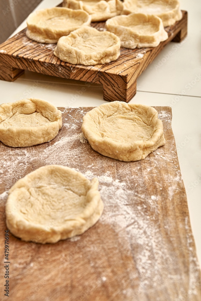 Pies forms of raw dough prepared for adding different fillers on rustic wooden boards on white table in kitchen close view