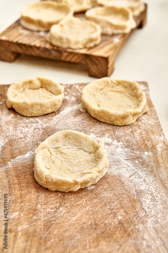 Pies forms of raw dough on rustic wooden boards on table