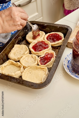 Senior woman fills raw pies with natural homemade berry jam cooking dessert at white table in kitchen extreme close view