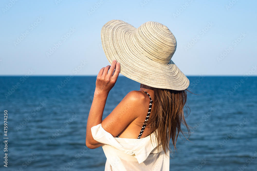 Young woman in hat on a cliff looks at the sea on a summer day.