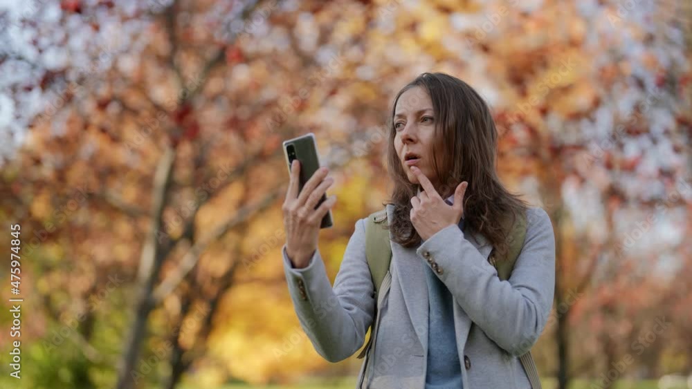 adult woman is calling by video conference in smartphone, walking in park in sunny fall day adult woman is calling by video conference in smartphone, walking in park in sunny fall day