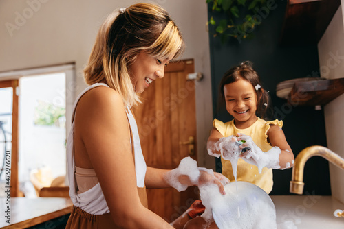 Happy mother and daughter washing dishes in the kitchen