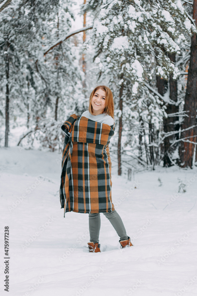A happy young girl, wrapped in a plaid plaid and basking on a walk in the winter forest. A walk in the Christmas holidays, selective focus A happy young girl, wrapped in a plaid plaid and basking on a walk in the winter forest. A walk in the Christmas holidays, selective focus