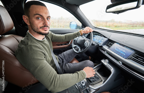 Portrait of handsome young man looking to the camera while driving modern car. © anatoliy_gleb