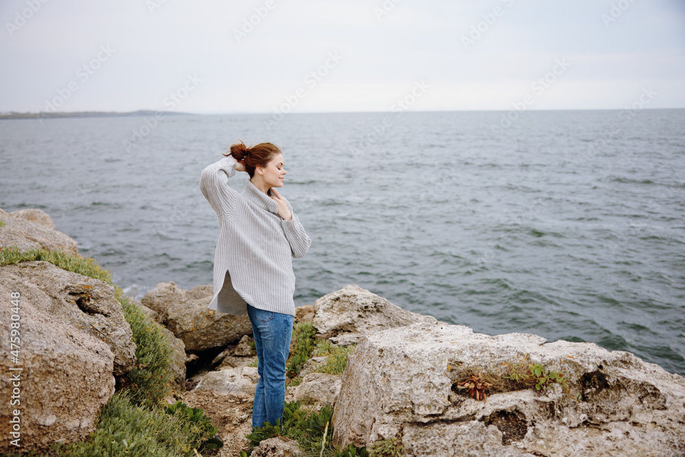 pretty woman in a gray sweater stands on a rocky shore nature Lifestyle