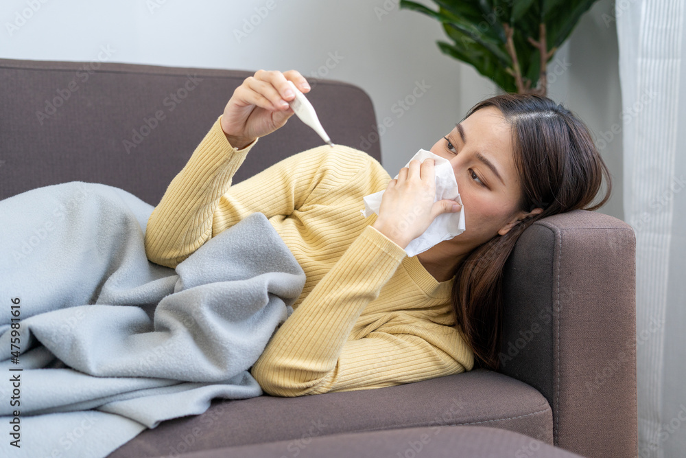 Asian woman sick with fever, runny nose and cough at home during the COVID-19 outbreak. Asian woman sick with fever, runny nose and cough at home during the COVID-19 outbreak.