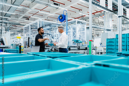 Coworkers having discussion by blue crates at factory production line photo