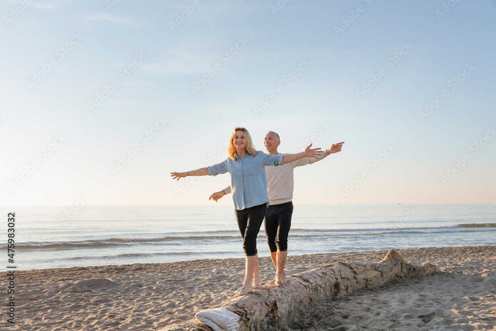 Couple with arms outstretched walking on tree log at beach Couple with arms outstretched walking on tree log at beach