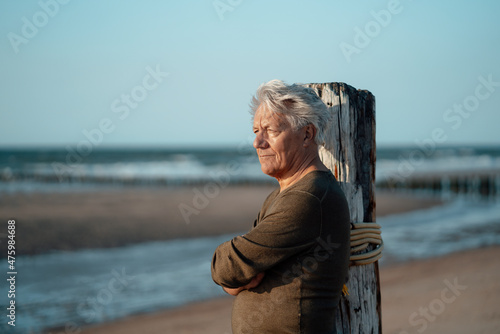 Senior man leaning on wooden post at beach photo